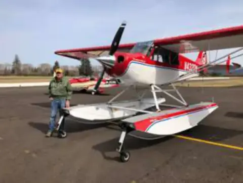 A man beside a red and white airplane on amphibious floats on the ramp