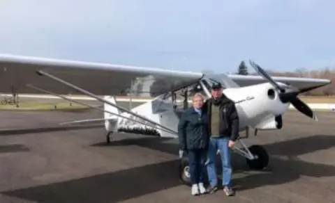 Two people standing beside a white high-wing airplane on the ramp