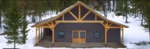 A log barn in the snow surrounded by trees