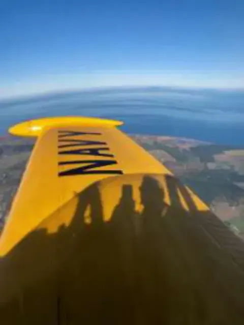 A yellow wing over a coastline seen from the cockpit