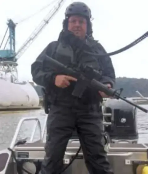 A man in winter gear holding a rifle on a boat deck
