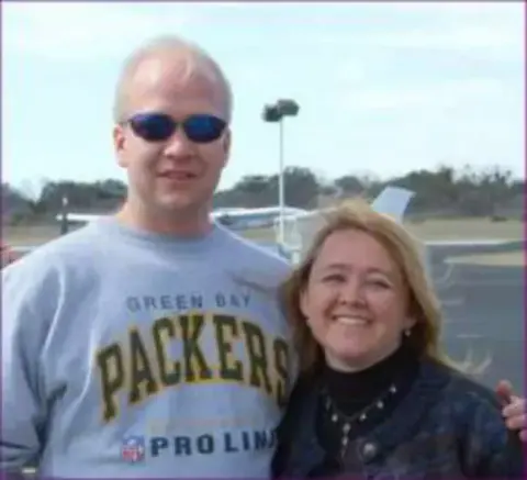 A smiling couple with an airport behind them