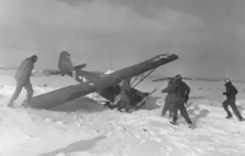 Soldiers gathered around a liaison airplane in the snow