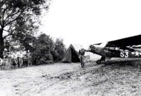 An old photo of a liaison airplane parked at a field camp