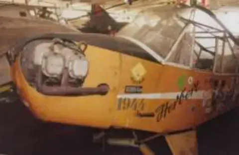 The nose of a yellow liaison airplane with nose art