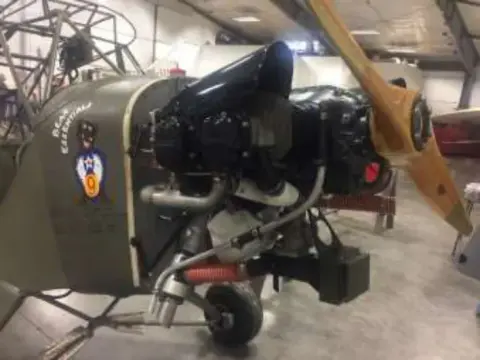 An olive drab liaison airplane being restored in a hangar