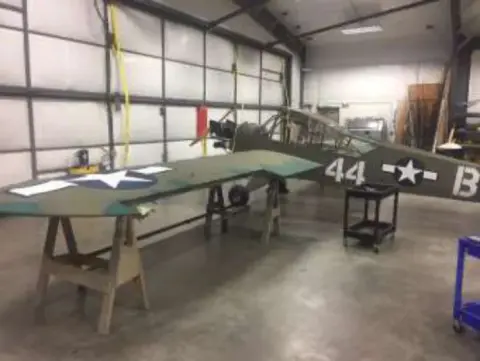 Wings and fuselage of an olive drab airplane in a restoration shop
