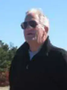 A white-haired man in sunglasses and a dark jacket, outdoors