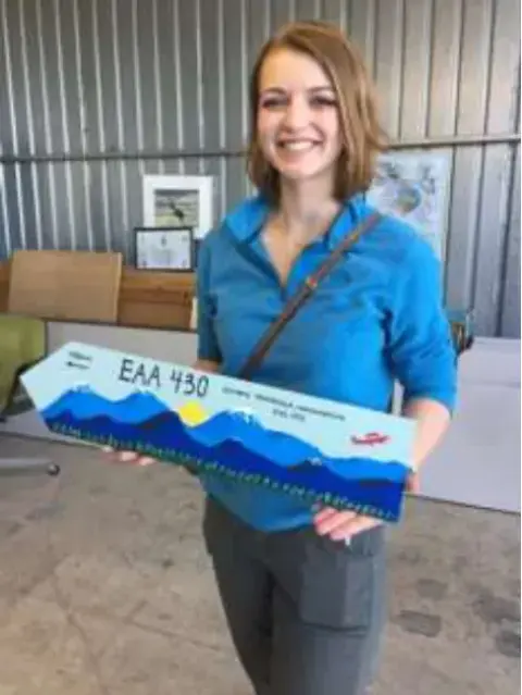 A young woman holding a painted wooden sign in a hangar