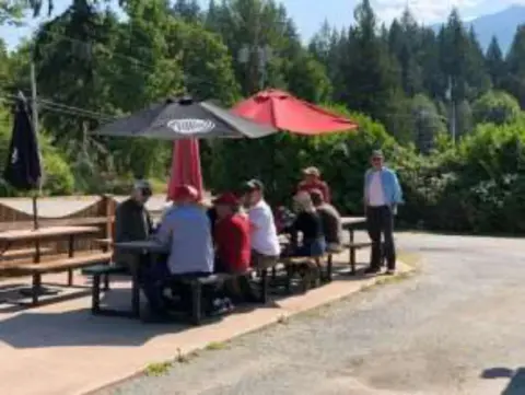 Members seated at picnic tables under umbrellas