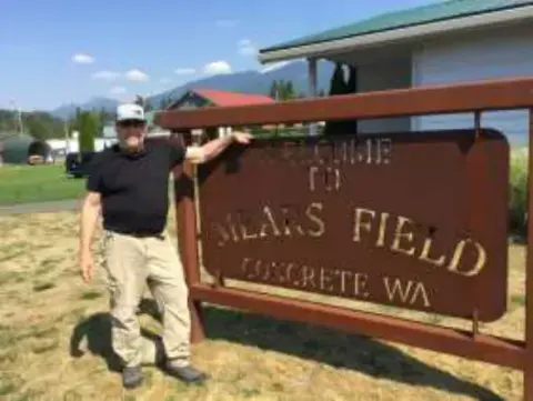 A man standing beside the Mears Field sign in Concrete, WA