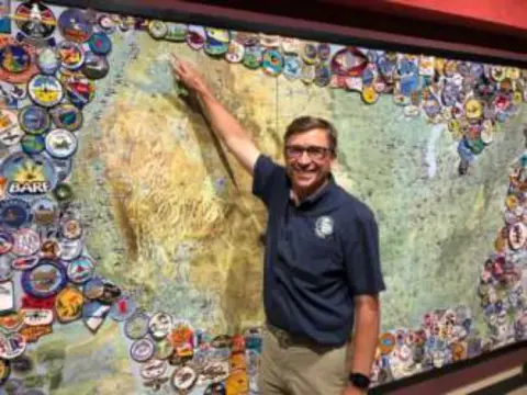A man pointing to a wall map covered with chapter patches