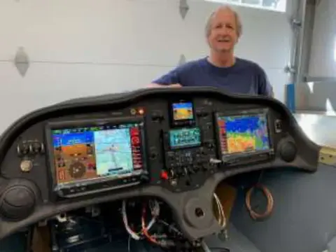 A smiling man standing behind an airplane instrument panel with three glass displays