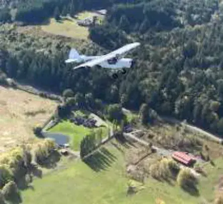 A small airplane flying over farmland and houses