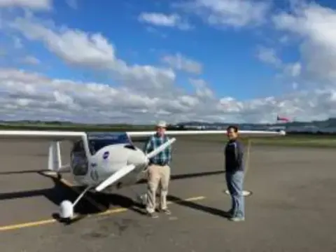 Two people next to a white low-wing airplane on the ramp