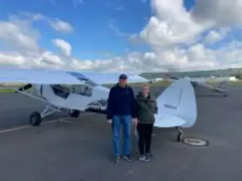 Two men standing in front of a high-wing airplane