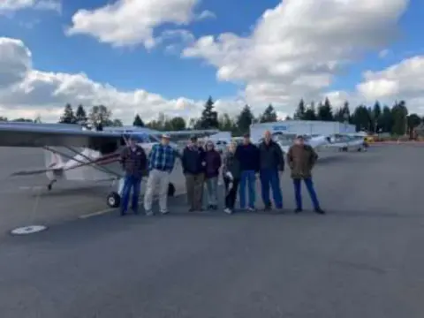 A group of members standing beside a parked airplane on the ramp