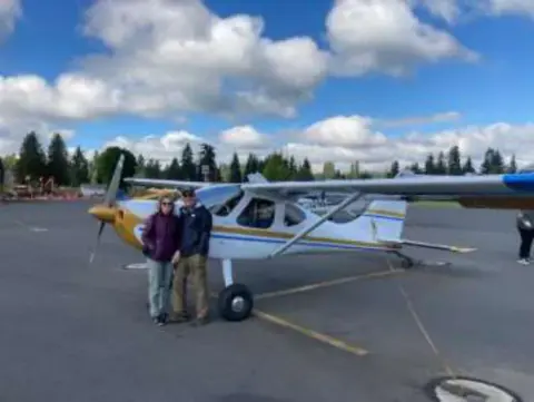 People standing by a high-wing airplane under a cloudy sky