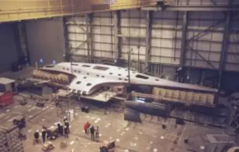 A large hangar with an aircraft under construction on the floor