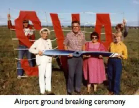 People posing with large red letters at an airport groundbreaking