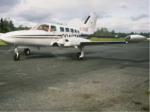 A white twin-engine airplane parked on grass