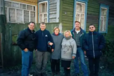 A family group standing in front of a wooden building