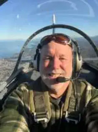 A pilot in a helmet taking a selfie in an open cockpit
