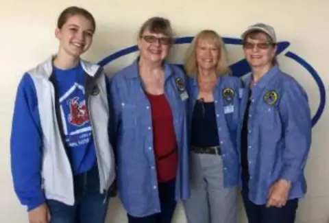 Madeline, Tracy, Skip and Lisa standing together in front of an EAA logo