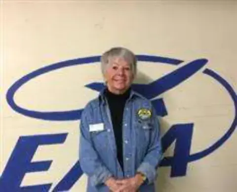 A woman standing in front of a large EAA logo