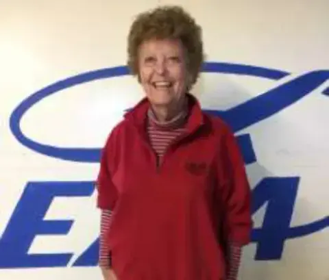 Emily, smiling in a red sweater in front of an EAA logo