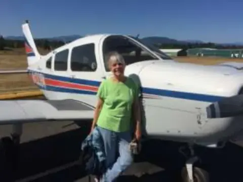 Mary Ann standing beside a white low-wing airplane on the ramp