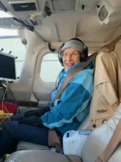 Leslie wearing a headset in the seat of an airplane cabin