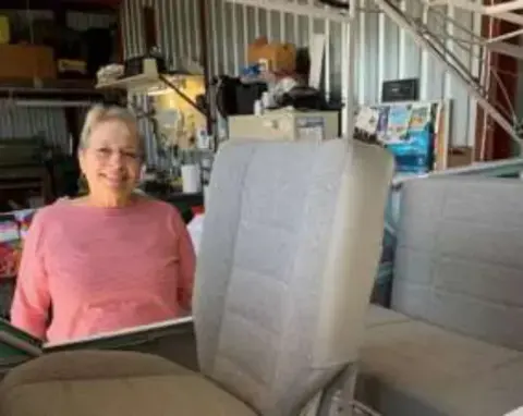 Jeanne in a pink top in a hangar workshop beside an airplane seat