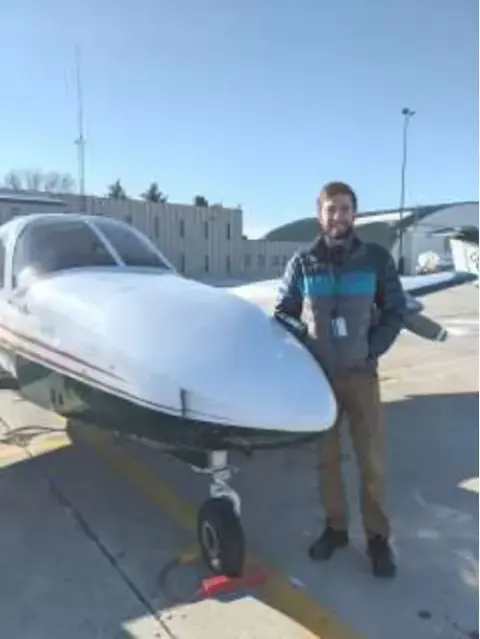 A man standing beside the nose of a white low-wing airplane