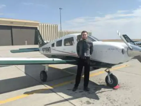 A man standing by the wing of a white low-wing airplane on the ramp