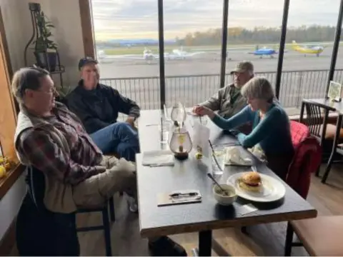 Members seated at a restaurant table by an airport window