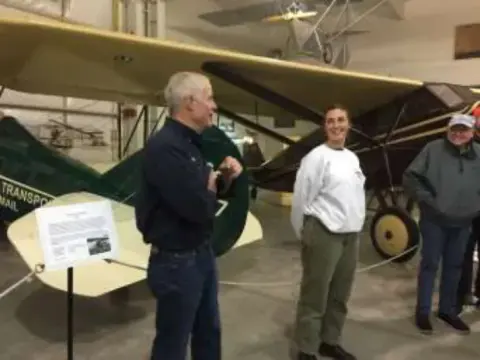Three men talking beside a vintage airplane in the museum