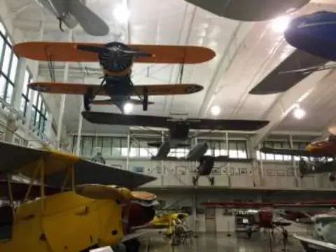 Biplanes hanging from the museum ceiling above yellow aircraft on the floor