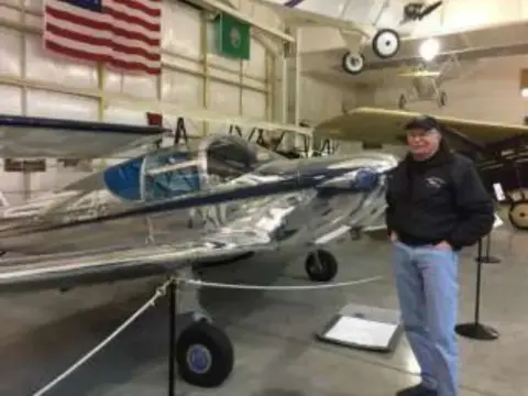 A man standing beside a polished silver airplane in the museum