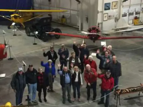 A group of members waving inside the museum hangar