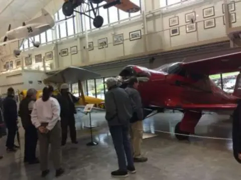 Members looking at a red cabin biplane in the museum
