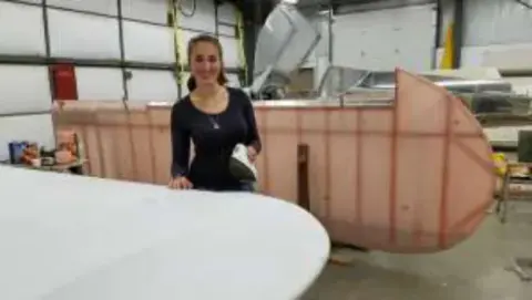 A young woman standing behind a fabric-covered fuselage in a shop