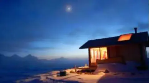 A lit cabin on a snowy mountainside at dusk