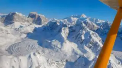 Snowy Alaska mountain peaks seen below a yellow wing strut