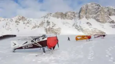Small airplanes on skis parked on a snowfield below mountains