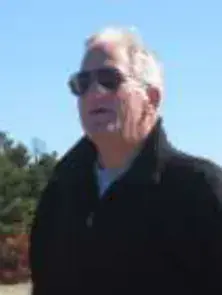 A white-haired man in sunglasses and a dark jacket, outdoors