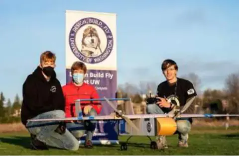 Students posing with a model airplane in front of a school banner