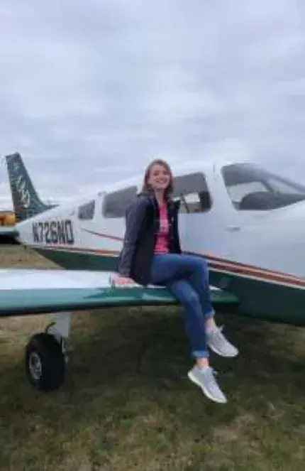 A woman sitting on the wing of a low-wing airplane