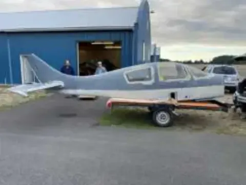 A low-wing homebuilt airplane fuselage on a trailer outside a hangar