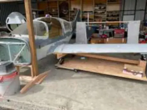 Airplane parts and a fuselage in a cluttered workshop